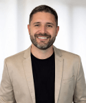 Retrato corporativo de Vinicius, CEO da Ferrbá, sorrindo com blazer bege e camiseta preta sobre fundo neutro
