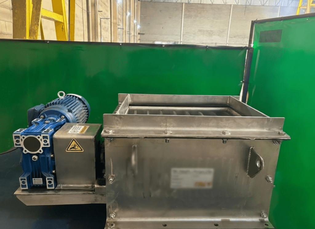 Moinho desgrumador industrial com carcaça em aço inoxidável e conjunto motoredutor azul acoplado, posicionado em área fabril com biombos de proteção.
