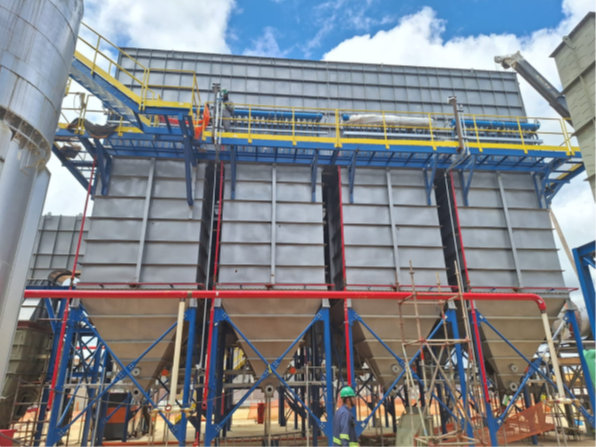 Filtro de mangas industrial de grande porte instalado em ambiente externo, com corpo metálico cinza, seções cônicas inferiores, estrutura de vigas azuis, plataforma de manutenção com guarda-corpo amarelo e tubulação vermelha de grande diâmetro.