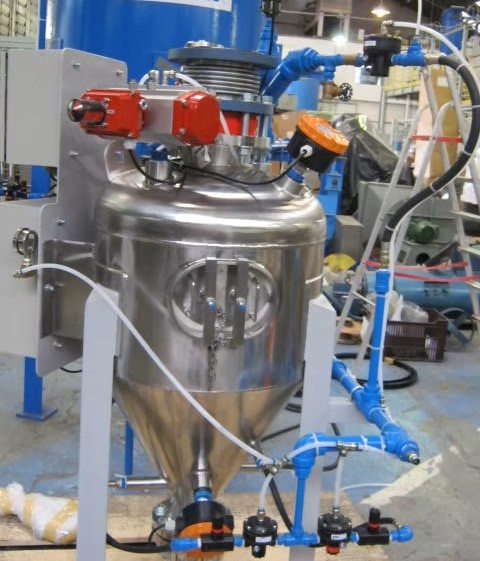 Sistema de transporte pneumático em fase densa composto por vaso de pressão em aço inoxidável com formato cônico inferior, válvulas de acionamento pneumático, instrumentação de controle e estrutura de sustentação metálica.